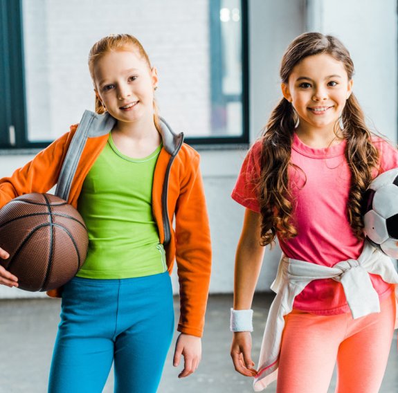Zwei Mädchen halten je ein Basketball und einen Fußball