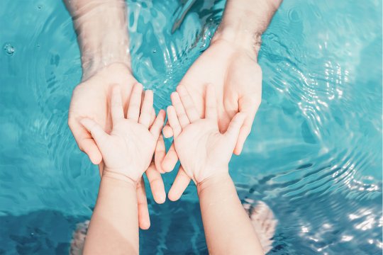 Baby und Erwachsene geben sich die Hand über dem Wasser