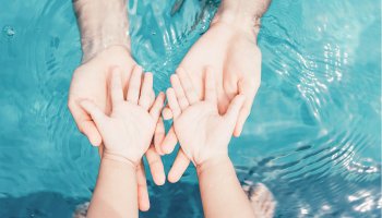Baby und Erwachsene geben sich die Hand über dem Wasser