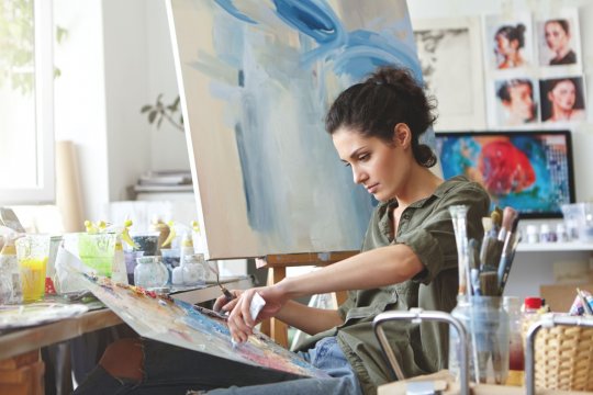 Frau sitzt vor einer Leinwand und malt