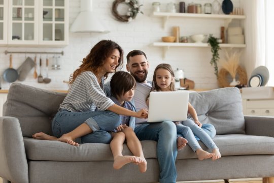 Eine Familie sitzt auf der Couch und schaut auf den Laptop Screen