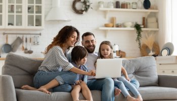 Eine Familie sitzt auf der Couch und schaut auf den Laptop Screen