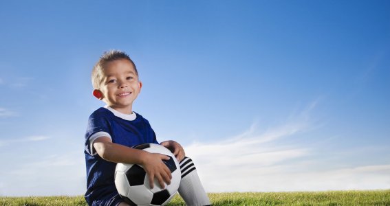 Junge sitzt lachend mit Fußball auf einer Wiese