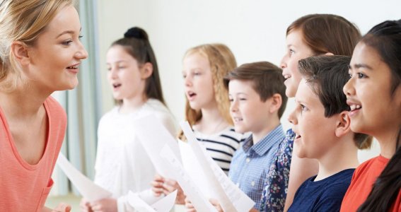 Kinder singen und die Lehrerin fördert sie.