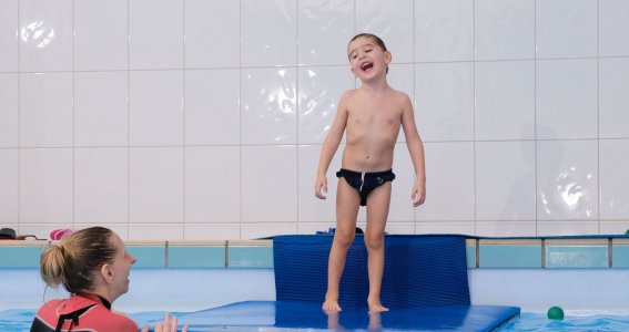 Kind auf einer Schwimmmatte und Schwimmlehrerin in Wasser 