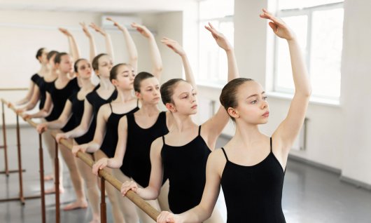 Mädchen stehen an einer Ballettstange und üben. 