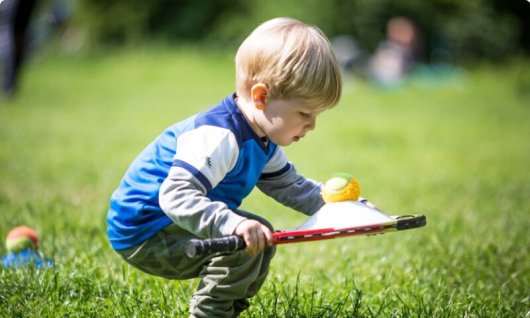Kleiner Junge hat einen Tennisschläger mit Tennisball in der Hand