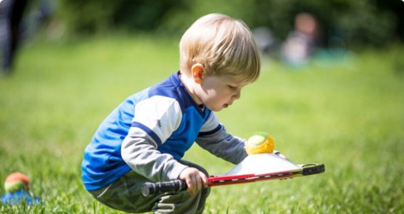 Kleiner Junge hat einen Tennisschläger mit Tennisball in der Hand