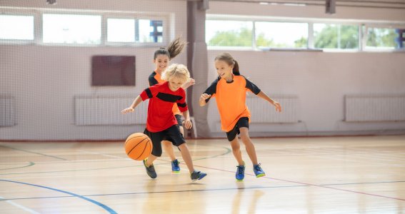 Drei Kinder spielen in der Turnhalle Basketball
