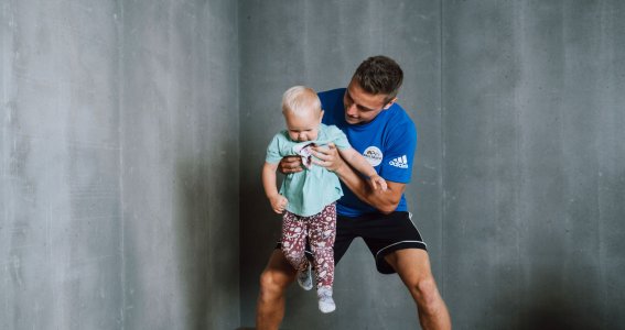 Ein junger Mann in Sportkleidung hält ein Kleinkind während Turnübungen in der Sporthalle