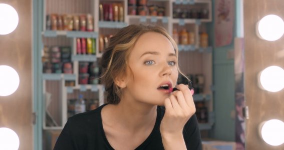 Eine junge Frau mit perfektem, dezenten Make-Up steht vor dem Spiegel und trägt Lippenstift auf