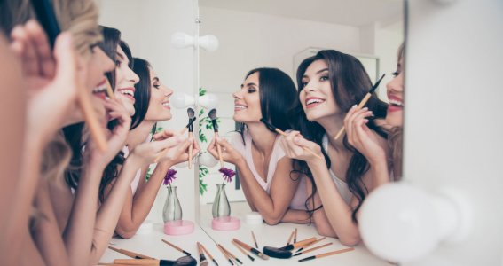 Drei lachende Frauen schminken sich vor einem Spiegel