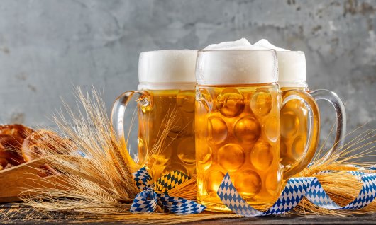 Drei große helle Gläser Bier inmitten Tischdekoration und Brezeln