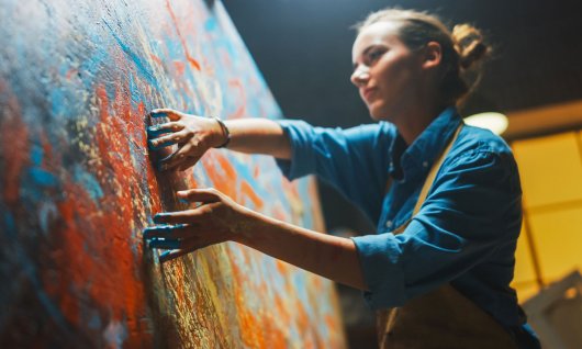 Eine Frau malt mit den Fingern ein abstraktes Bild auf die Leinwand