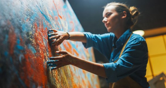 Eine Frau malt mit den Fingern ein abstraktes Bild auf die Leinwand