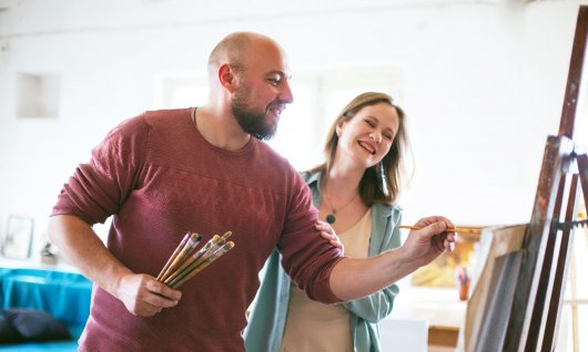 Ein junges Paar malt gemeinsam auf eine kleine Leinwand