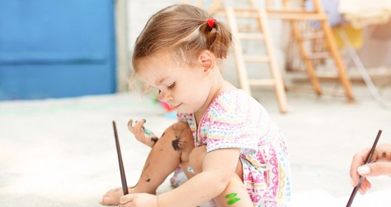 Mit Farbe bekleckertes Kind sitzt auf dem Boden und malt ein Bild