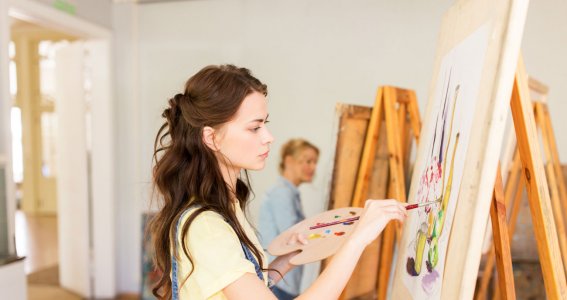 Frau malt an Staffelei mit Farbpalette
