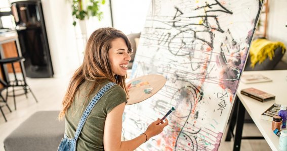 Frau malt lachend auf einer großen Leinwand