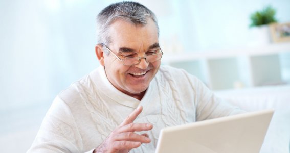 Ein lachender älterer Mann sitzt vor dem Laptop
