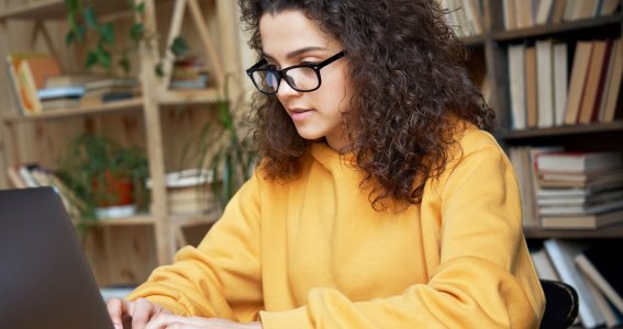 Eine junge Frau mit lockigen Haaren sitzt vor dem Laptop und schreibt auf der Tastatur