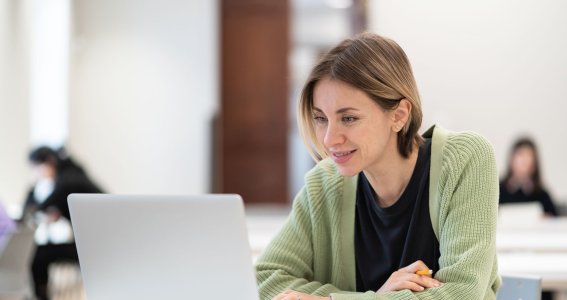 Eine Frau sitzt in einem großen Raum vor dem Laptop