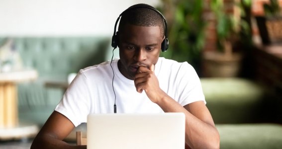 Ein junger Mann mit Kopfhörern schaut konzentriert in seinen Laptop