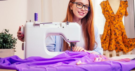 Frau sitzt an einer Nähmaschine und näht Stoff. 