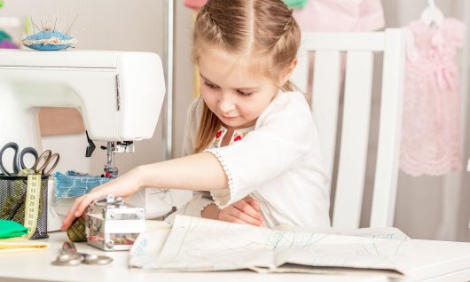 Mädchen lernt an einer Nähmaschine nähen.