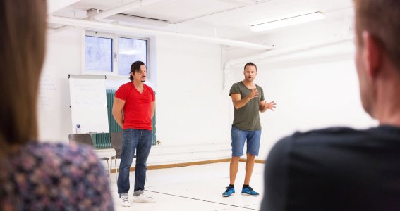2 Männer bringen im Raum Schülern Schauspielen bei.