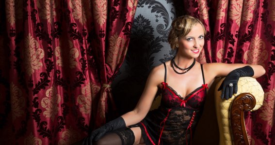 Eine Frau in schwarz-rotem Burlesque Outfit sitzt auf einem Lehnstuhl