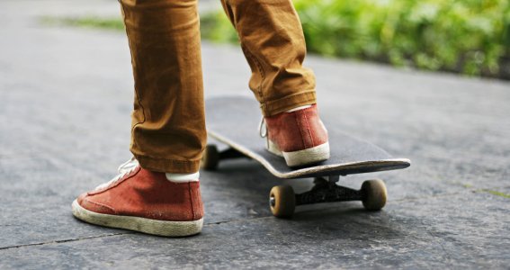 Männerfüße in rot-braunen Sneakers fahren Skateboard