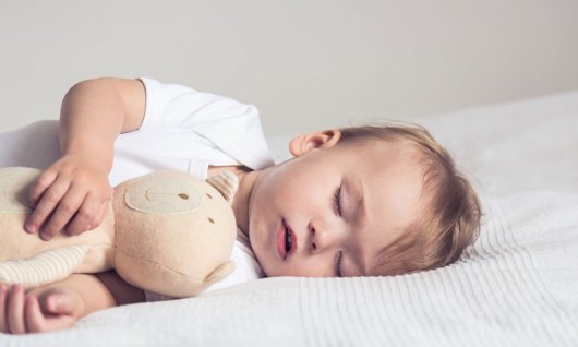 Baby schläft im Bett mit Kuscheltier. 