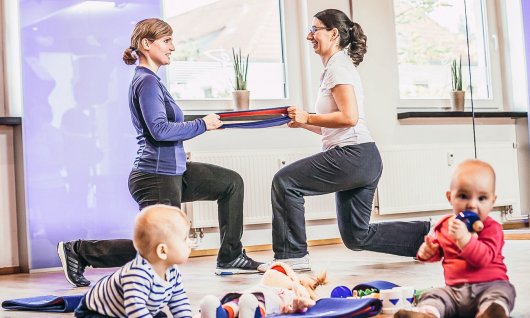 Mütter machen zusammen Sport und Babys spielen währenddessen gemeinsam 