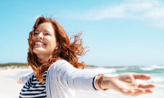 Eine strahlende Frau mit ausgestreckten Armen auf dem Strand
