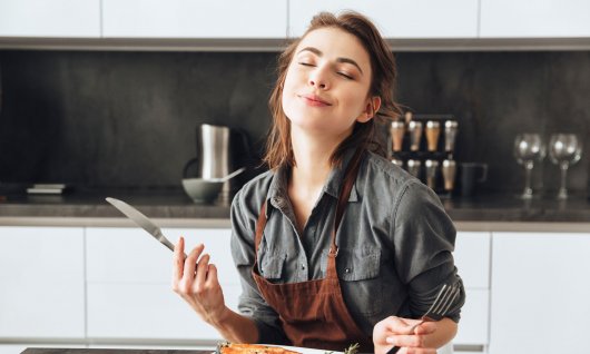 Eine junge Frau isst mit Genuss ein Stück Fisch und Gemüse