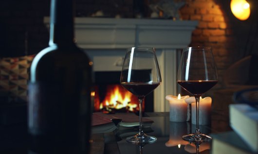 Zwei Rotweingläser stehen auf dem Tisch und Kamin ist im Hintergrund