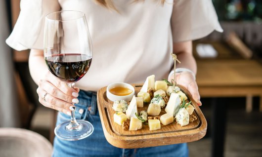 Frau hält ein Rotweinglas und eine Käseplatte in der Hand.