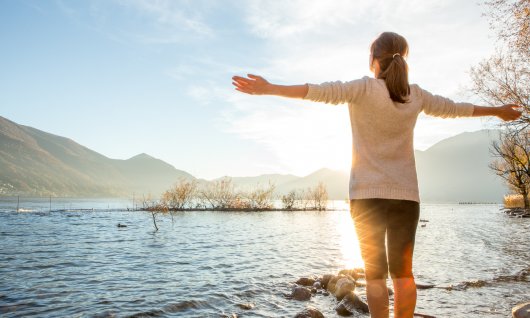 Frau steht am See und genießt die Natur und die Sonne