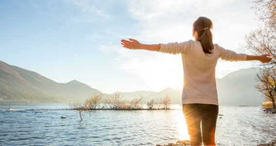 Frau steht am See und genießt die Natur und die Sonne