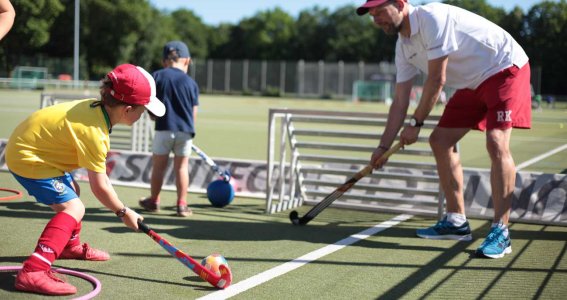 Trainer und Kind üben Feldhockey