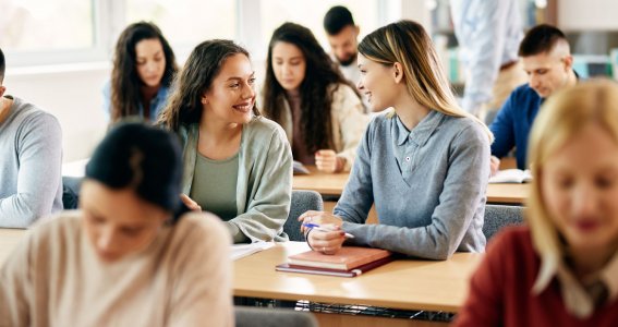 Erwachsene sitzen im Klassenzimmer am Tisch. 