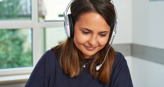 Frau sitzt mit Headset vor dem Computer