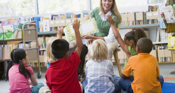 Lehrerin zeigt den Kindern ein Buch die am Boden sitzen. 