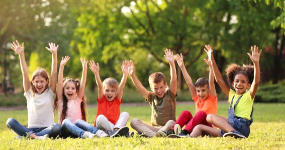 Kinder sitzen auf der Wiese und halten Hände in die Luft