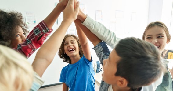 Kinder stehen im Klassenzimmer und klatschen sich die Hände in der Luft