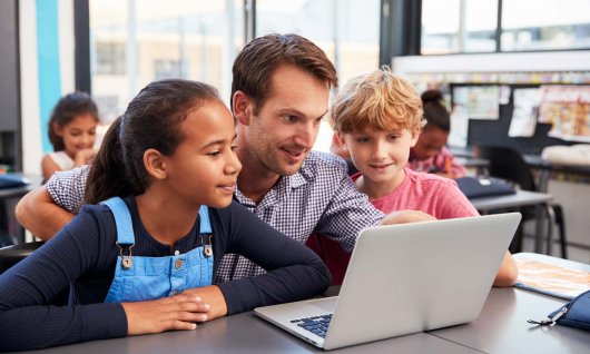 Kinder sitzen mit Lehrer vor Laptop