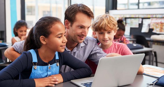 Kinder sitzen mit Lehrer vor Laptop