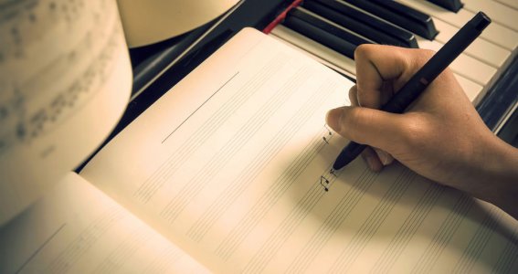 Noten in ein Notenheft schreiben, das auf einem Klavier liegt