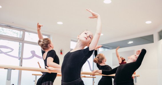 Kleine Tänzerinnen machen Übungen an der Ballettstange
